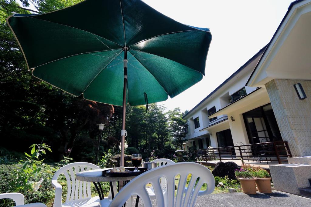 a table with a green umbrella and white chairs at Teiensaryo Yamanakako in Yamanakako