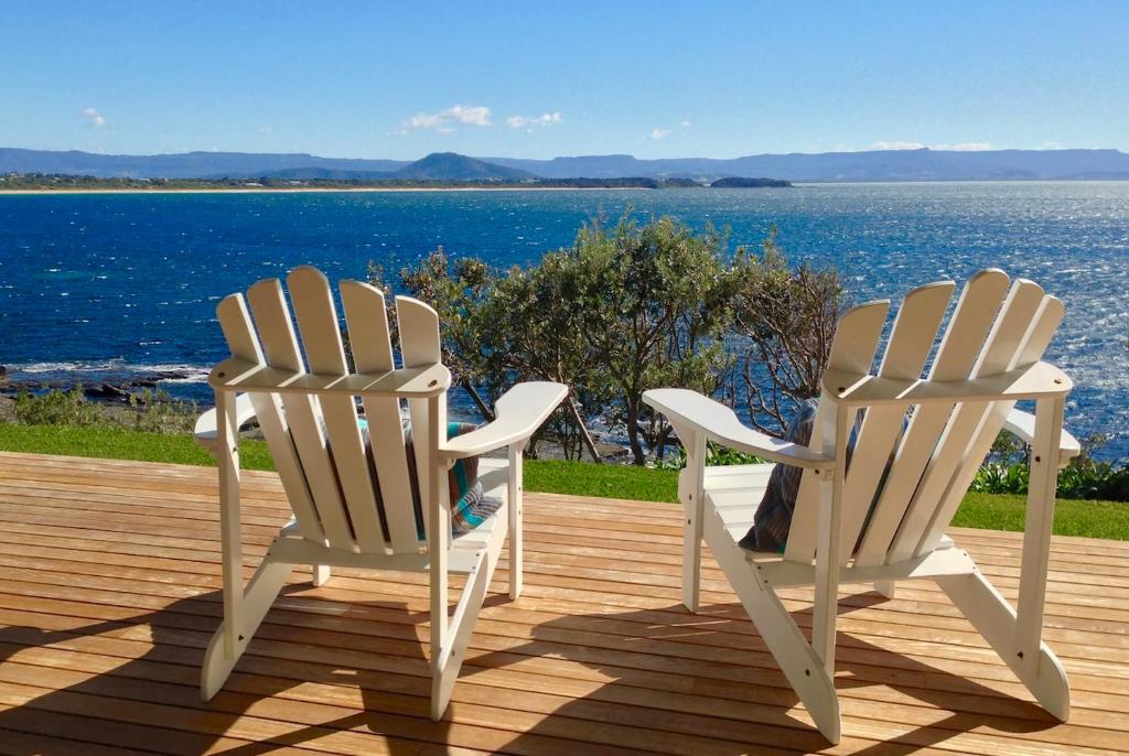 two white chairs sitting on a deck overlooking the water at 'South Pacific' - Luxury Oceanfront at Culburra! in Culburra Beach