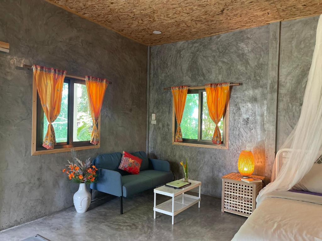 een woonkamer met een bank en 2 ramen bij Big hug home-Forest House in Ban Takhrai