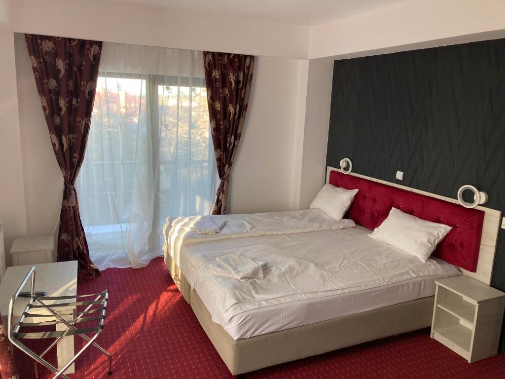 a bedroom with a bed with a red headboard and a window at Hotel Rudo in Predeal