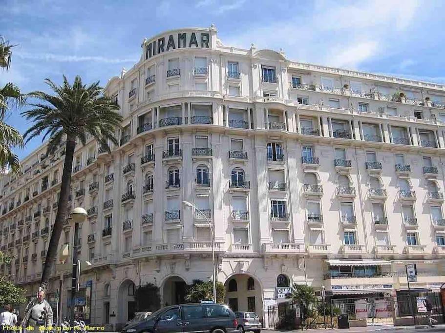 un grand bâtiment blanc avec un palmier en face dans l'établissement Mythique Miramar Cannes Croisette Terrasse Clim Parking Wifi, à Cannes