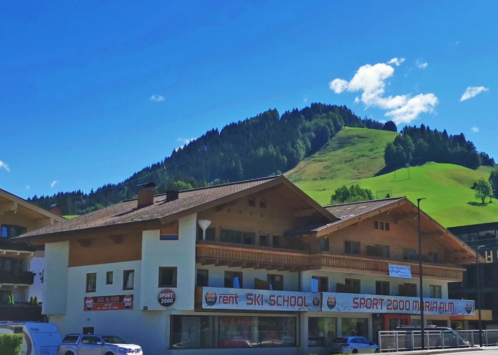 a large building with a green hill in the background at Alpin Apartments in Maria Alm am Steinernen Meer