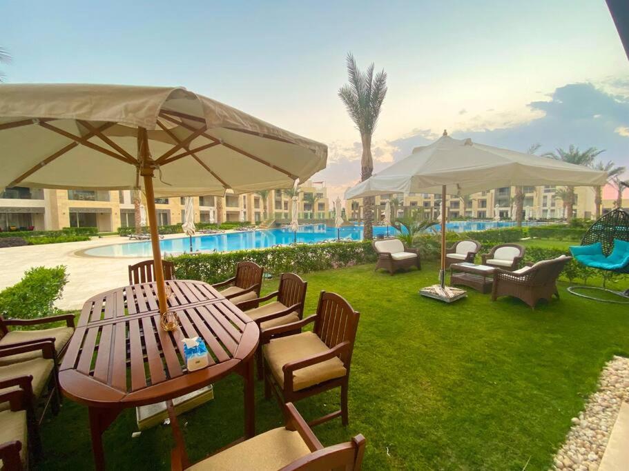 Glamorous 2BR/ Free Beach & Pool Access @ Mangroovy, El Gouna في الغردقة: طاولة وكراسي مع مظلات بجانب المسبح