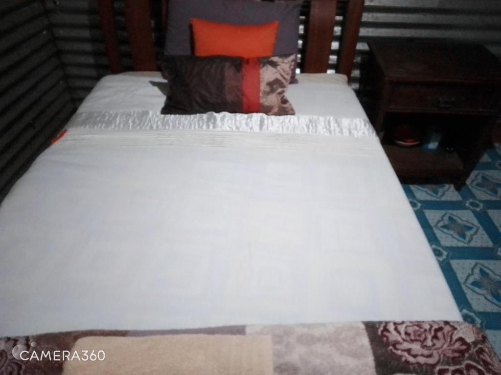 Una cama con sábanas blancas y almohadas. en Cosy budget Single room en Nairobi
