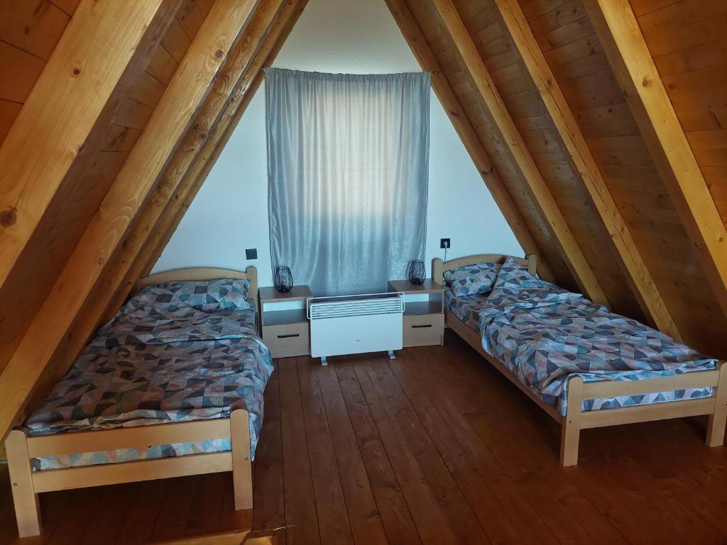 two beds in a attic room with a window at Vikendica Šumski mir Romanija-Sokolac-Sarajevo-Jahorina in Sokolac