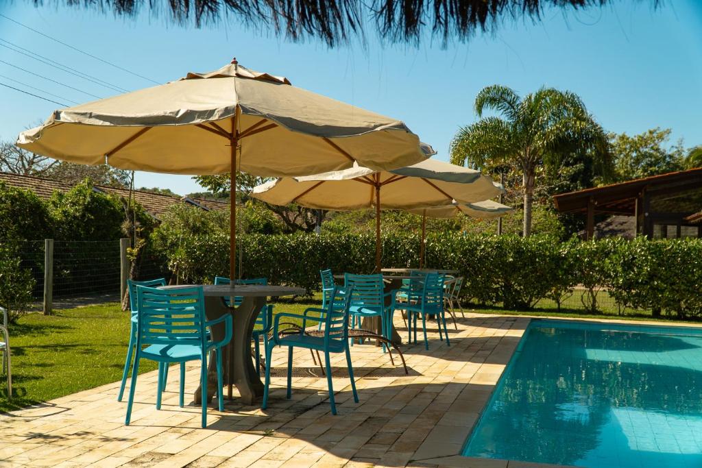 duas mesas e cadeiras com guarda-sóis ao lado de uma piscina em Pousada Dunasol Floripa em Florianópolis