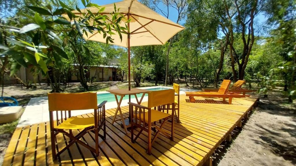 une terrasse en bois avec une table, des chaises et un parasol dans l'établissement Hostería Jasy, à Colonia Carlos Pellegrini