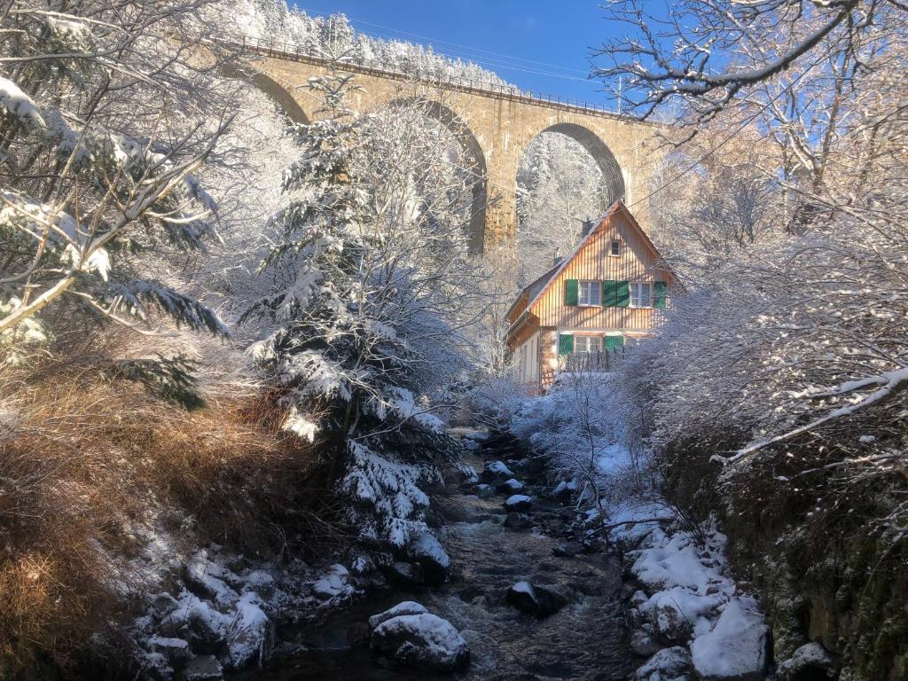 un pont sur un ruisseau avec une maison dans la neige dans l'établissement Ravenna Lodge, à Breitnau