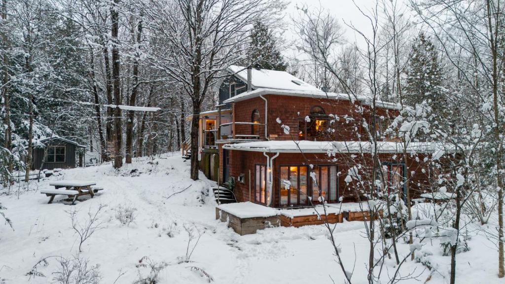 a house is covered in snow with a picnic table at Auberge Yoga Salamandre in Lac-Brome