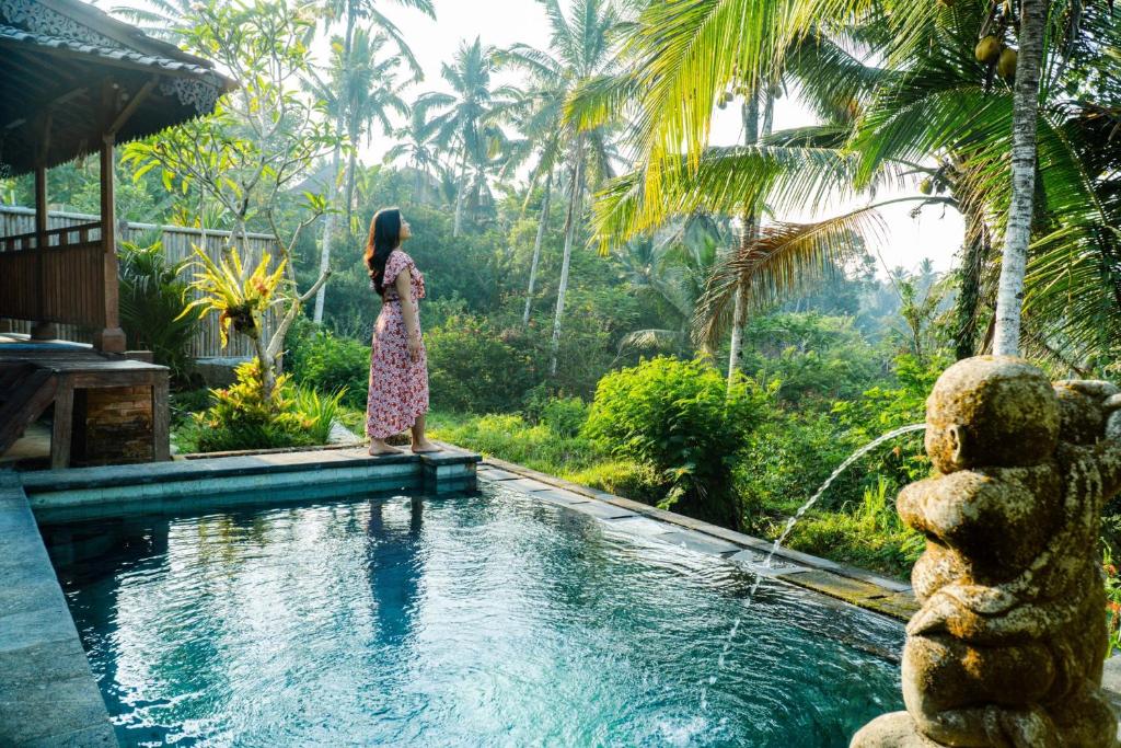 una mujer con un vestido de pie junto a una piscina en Tirta Jenar Villas en Tegalalang