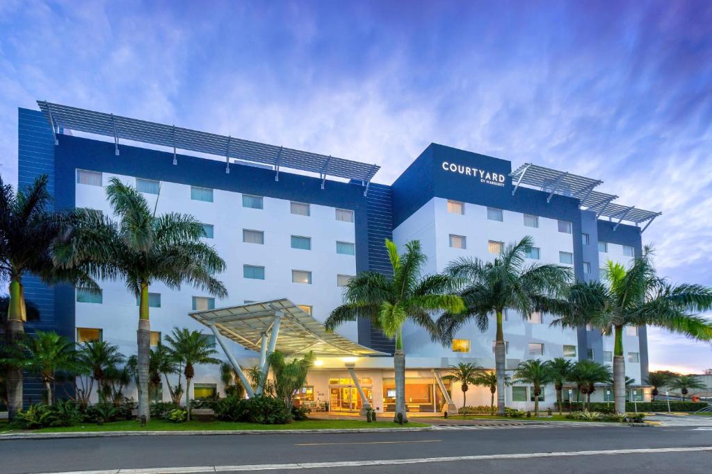 un hôtel avec des palmiers devant lui dans l'établissement Courtyard by Marriott San Jose Airport Alajuela, à Alajuela