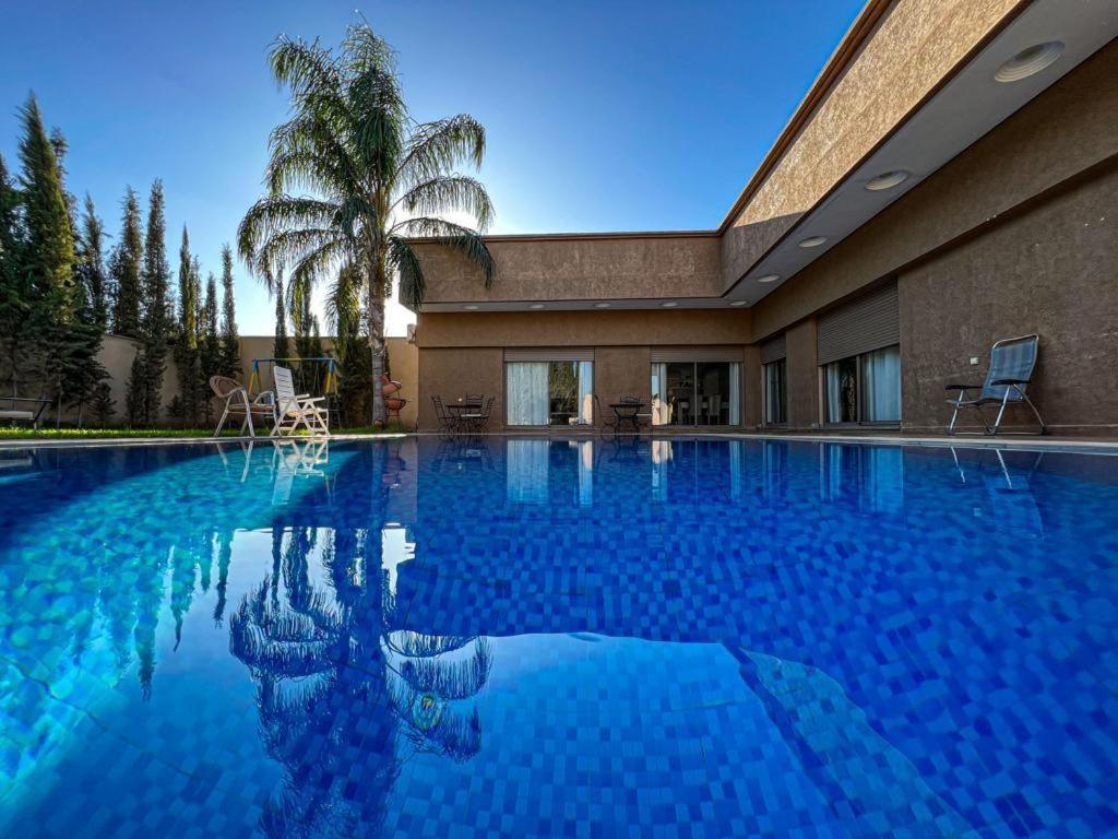 una gran piscina con una palmera y un edificio en Agafay villa, en Marrakech