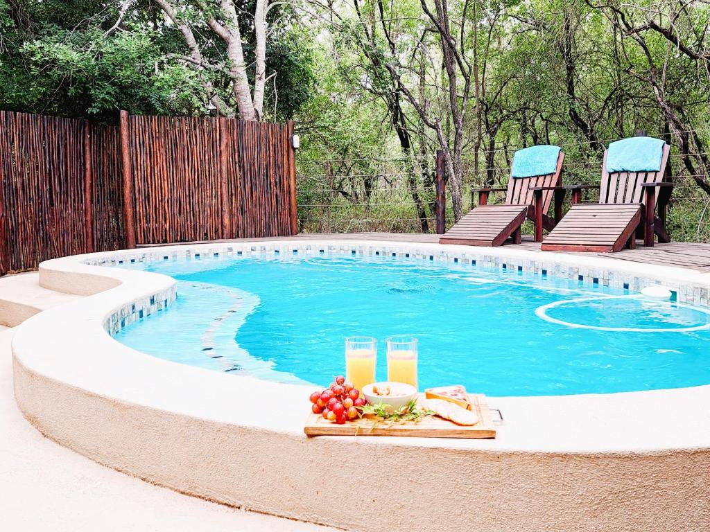 a pool with two chairs and a table with drinks at Treetops Marloth Park in Marloth Park