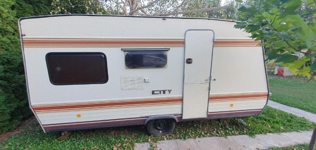 a white trailer is parked in the grass at Kamp prikolica četvorokrevetna in Crnča