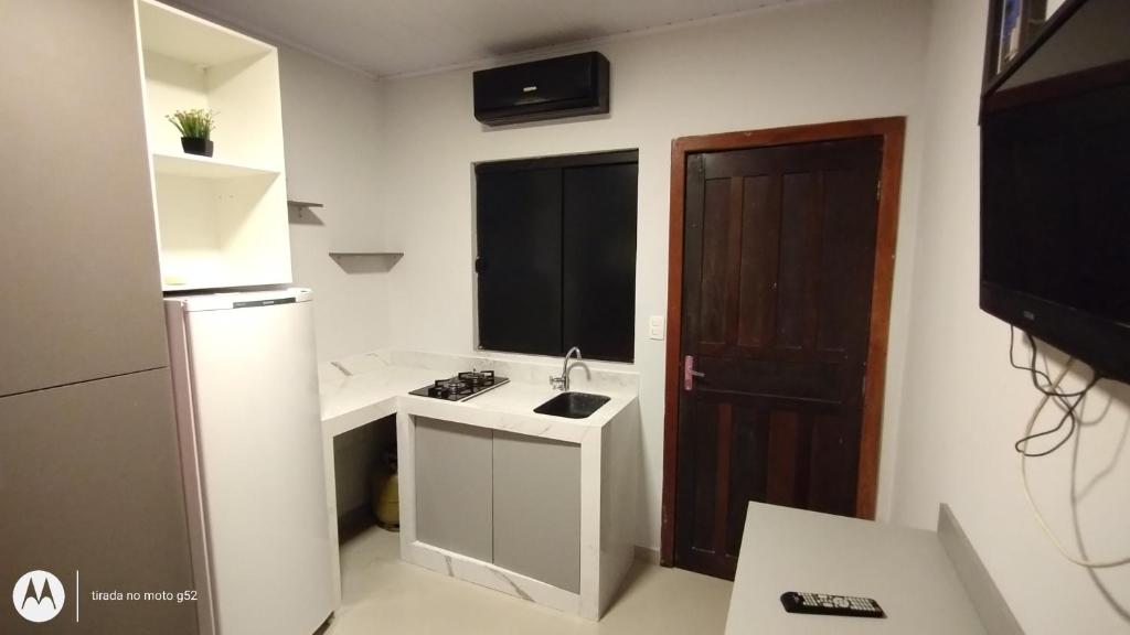 una pequeña cocina con fregadero y nevera. en Quitinete compacta, en Balneário Camboriú