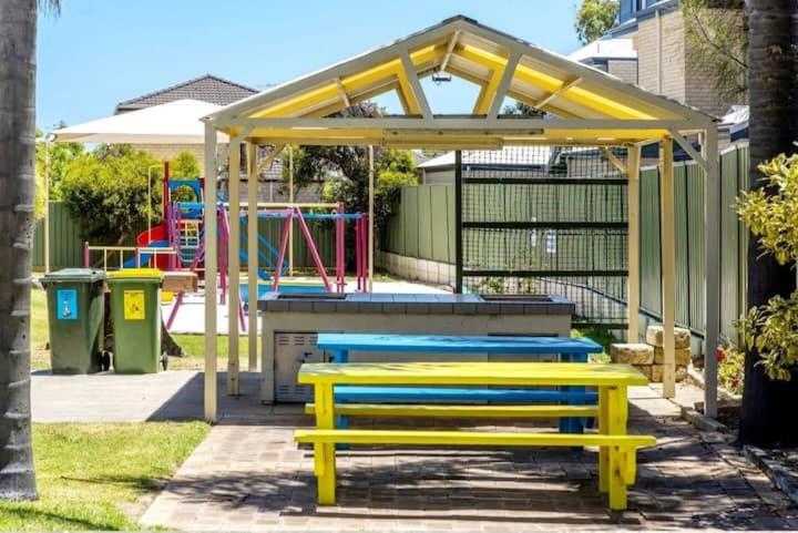 a playground with yellow and blue benches in a park at Just Beachy Loft Villa in Mandurah