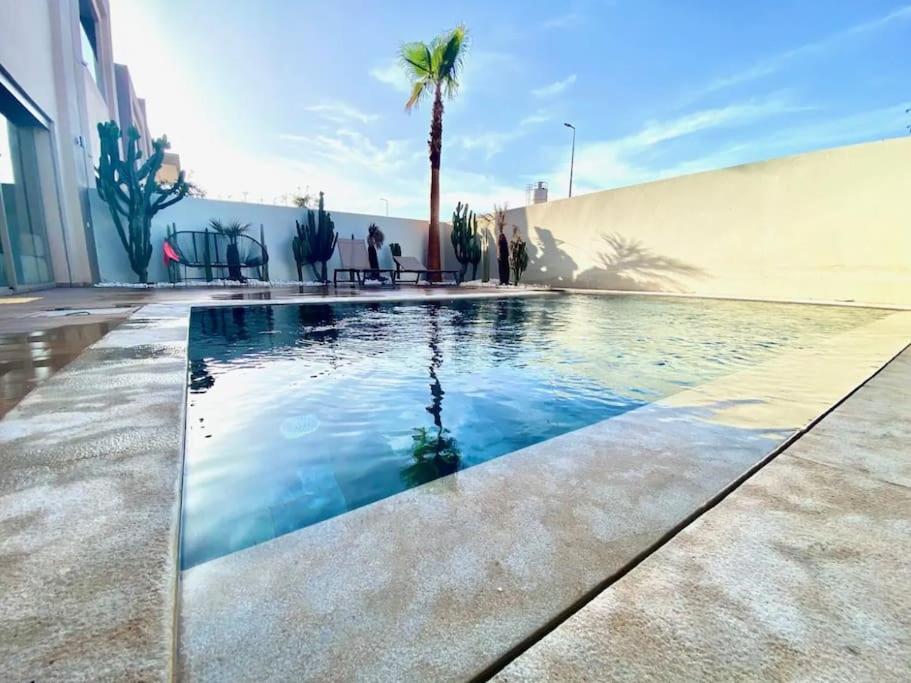 a swimming pool in front of a building with a palm tree at Villa California vue Atlas avec piscine chauffée in Marrakesh