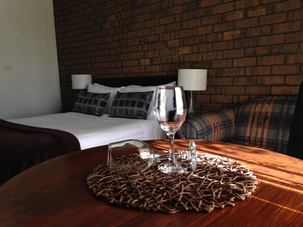 a table with a wine glass and a bed at City Colonial Motor Inn in Mildura