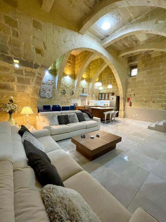 a living room with white couches and a stone wall at Daner Ta’ Pantu House in Kerċem