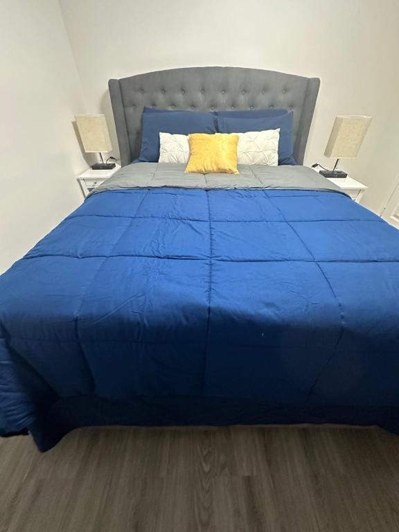 a large bed with a blue comforter and two lamps at Walkout basement apartment in Mississauga