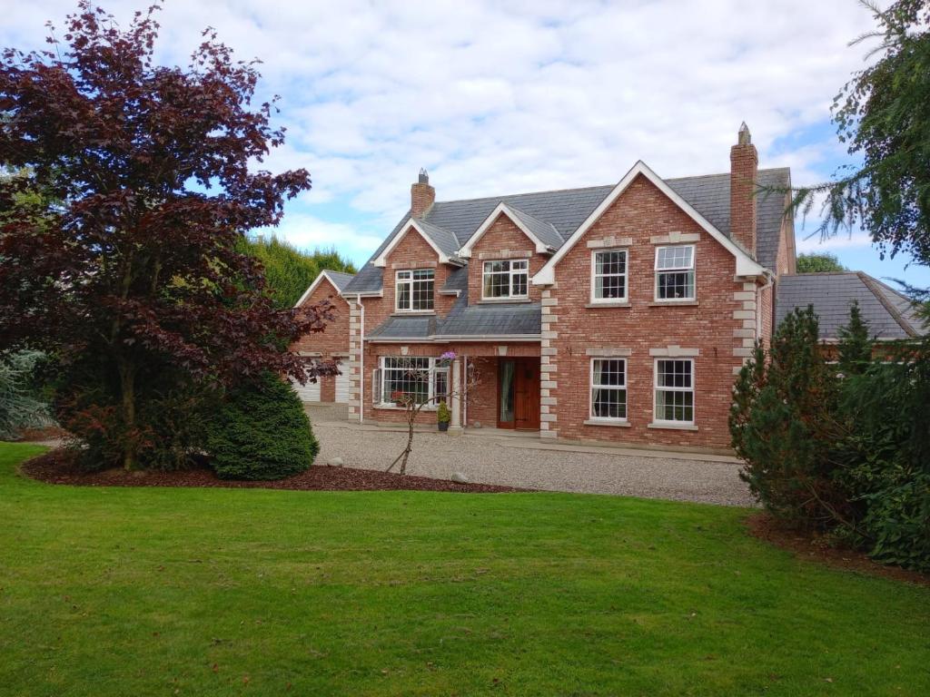 een groot bakstenen huis met een groene tuin bij Tullynacrunat Lodge in Castleblayney