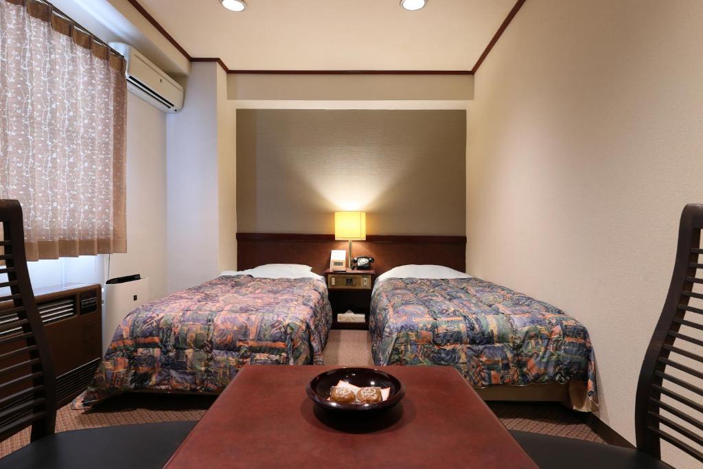 a hotel room with two beds and a table at Hotel Takamatsu in Kusatsu