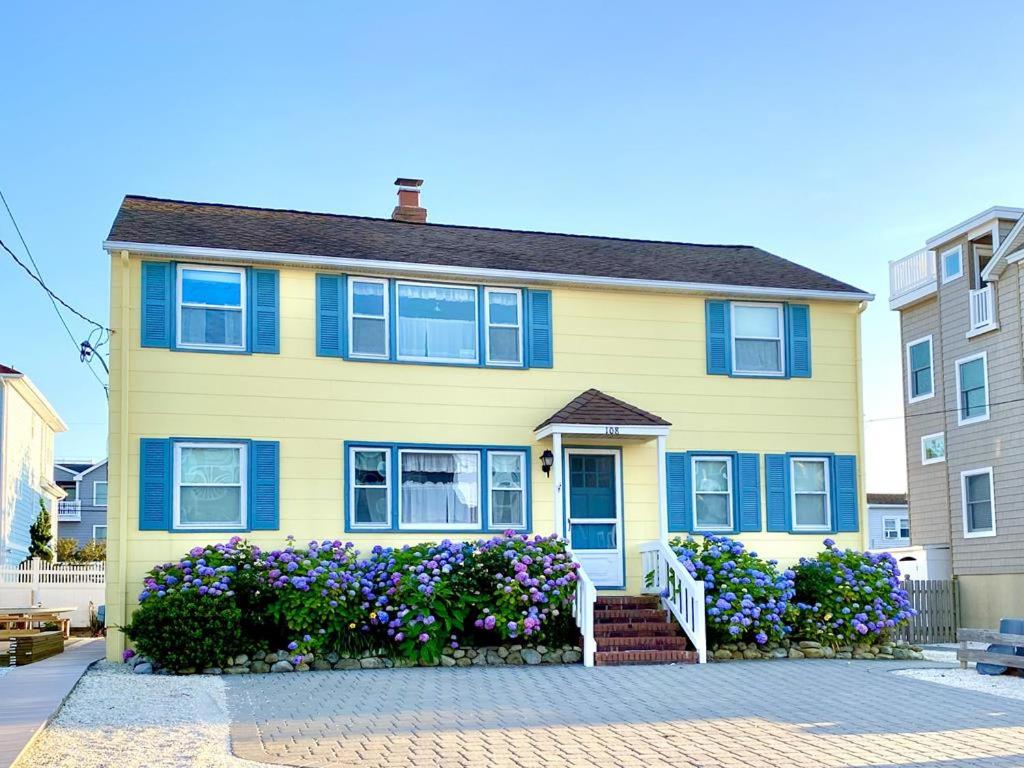 une maison jaune avec des fenêtres bleues et des fleurs violettes dans l'établissement Affordable Vacation Rental On Lbi, à Brighton Beach