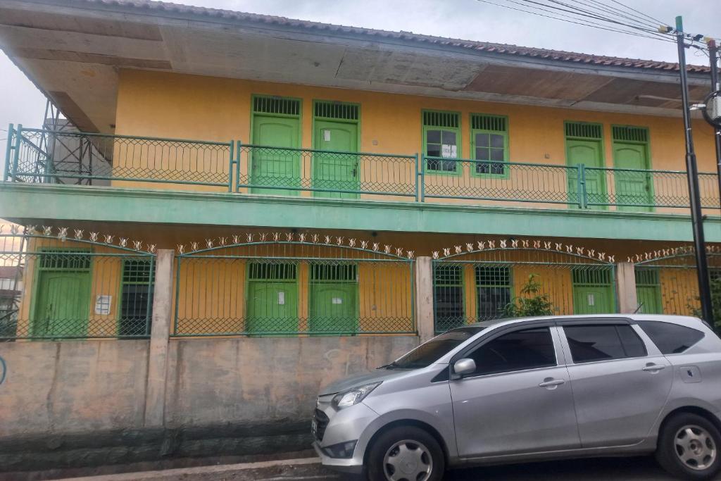 een zilveren busje geparkeerd voor een gebouw met groene deuren bij SPOT ON 93539 Juan Guest House in Purwokerto