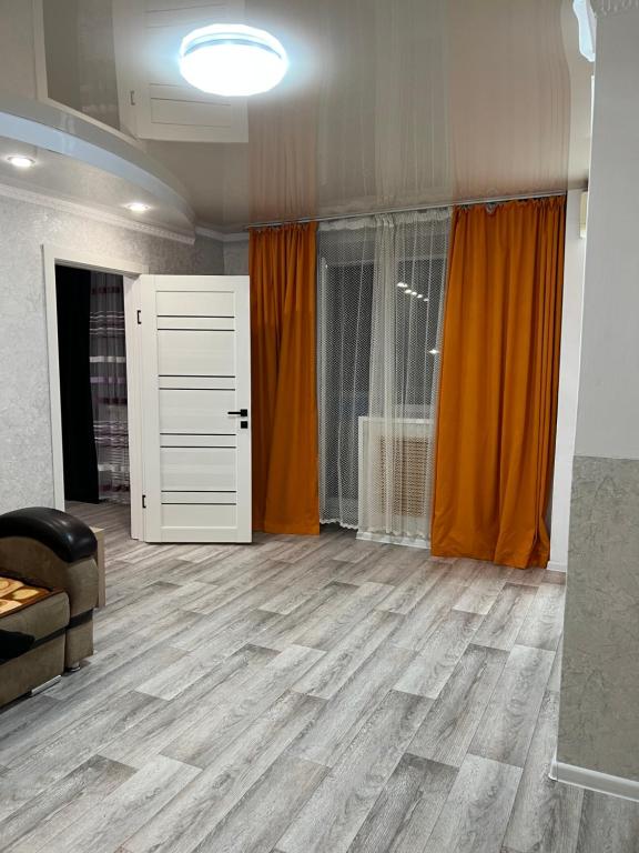 uma sala de estar com pisos em madeira e cortinas cor de laranja em Апартаменты Экибастуз em Ekibastuz