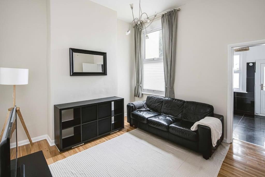 a black leather couch in a living room with a mirror at Super Stylish 1BD Flat with Garden in Leytonstone in London