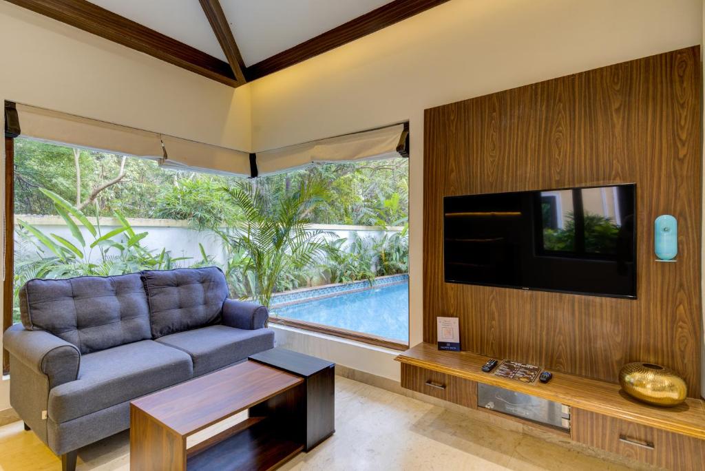 sala de estar con sofá, TV y piscina en Tropical villa by Happyinch, en Saligao