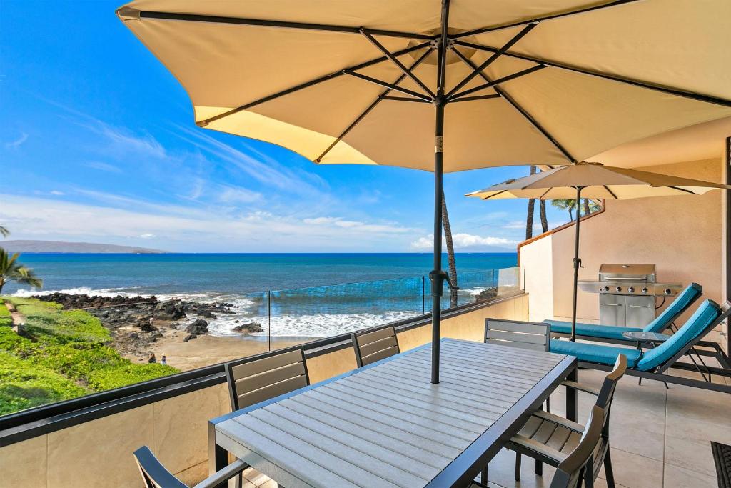 a table and chairs with an umbrella and the beach at Makena Surf G-201 - End Unit, Panoramic Views, AC! in Wailea