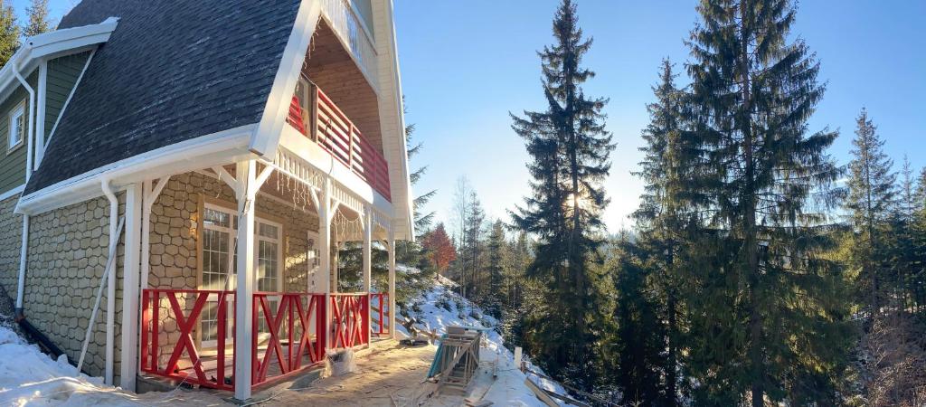 a house with a red front porch in the snow at Апартементи для 4 людей з окремим входом та терасою - весь перший поверх нового котеджу Freeman Bukovel - поряд витяг R1 in Bukovel