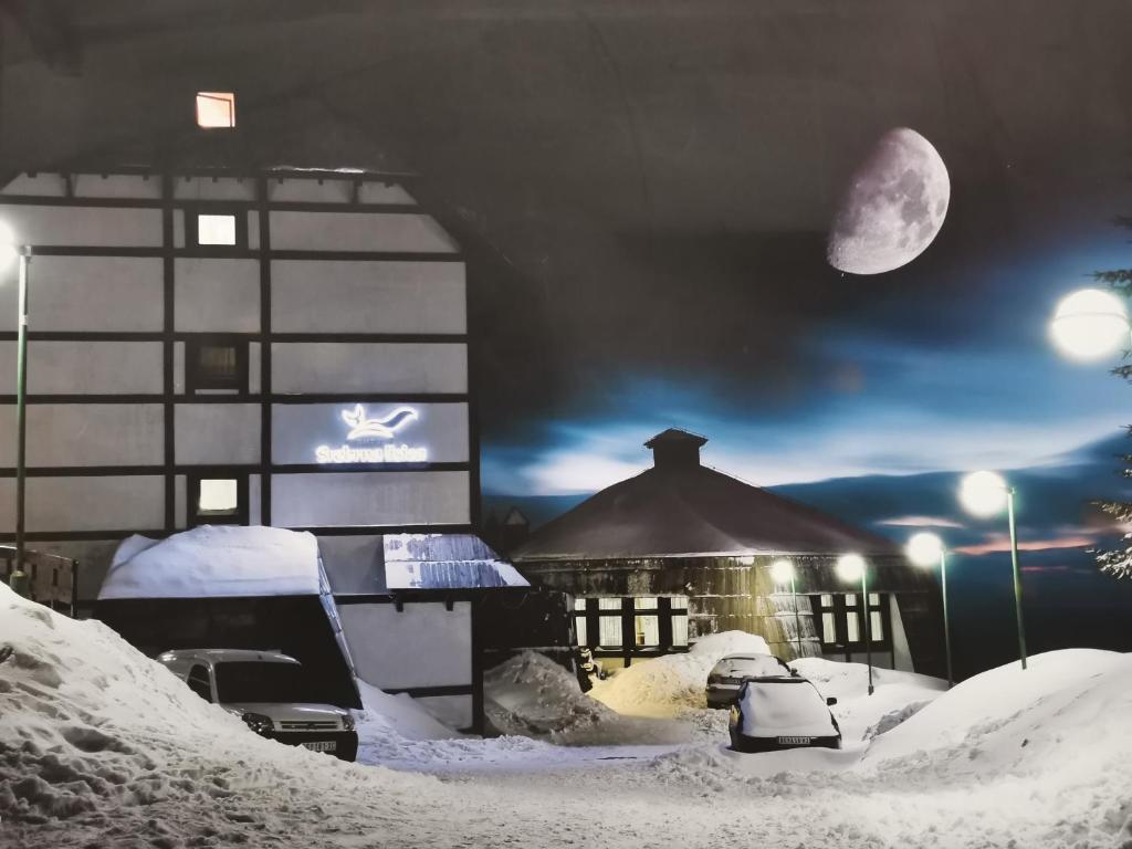 un edificio cubierto de nieve por la noche con luna en Hotel Srebrna lisica, en Kopaonik