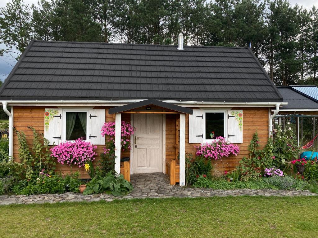 a small house with a black roof and flowers at Różana Zagroda Agroturystyka in Osiek