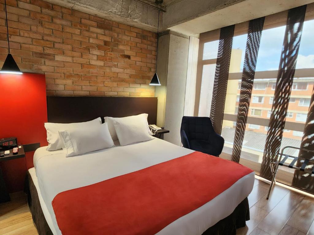 Habitación de hotel con cama, silla y ventana en Hotel 5 Elementos Corferias by HBP en Bogotá