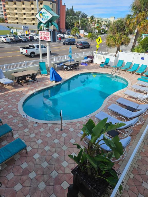 a swimming pool with lounge chairs and a parking lot at Oasis Palms Resort in St. Pete Beach