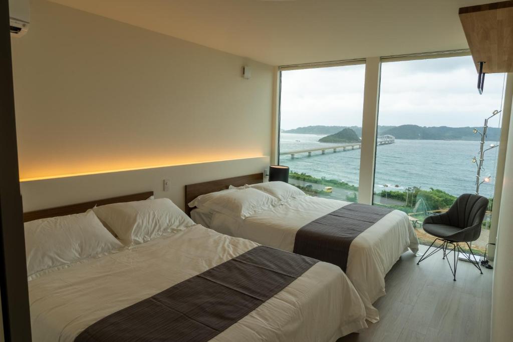 two beds in a room with a view of the ocean at ヴィラミクリ角島 in Takibe