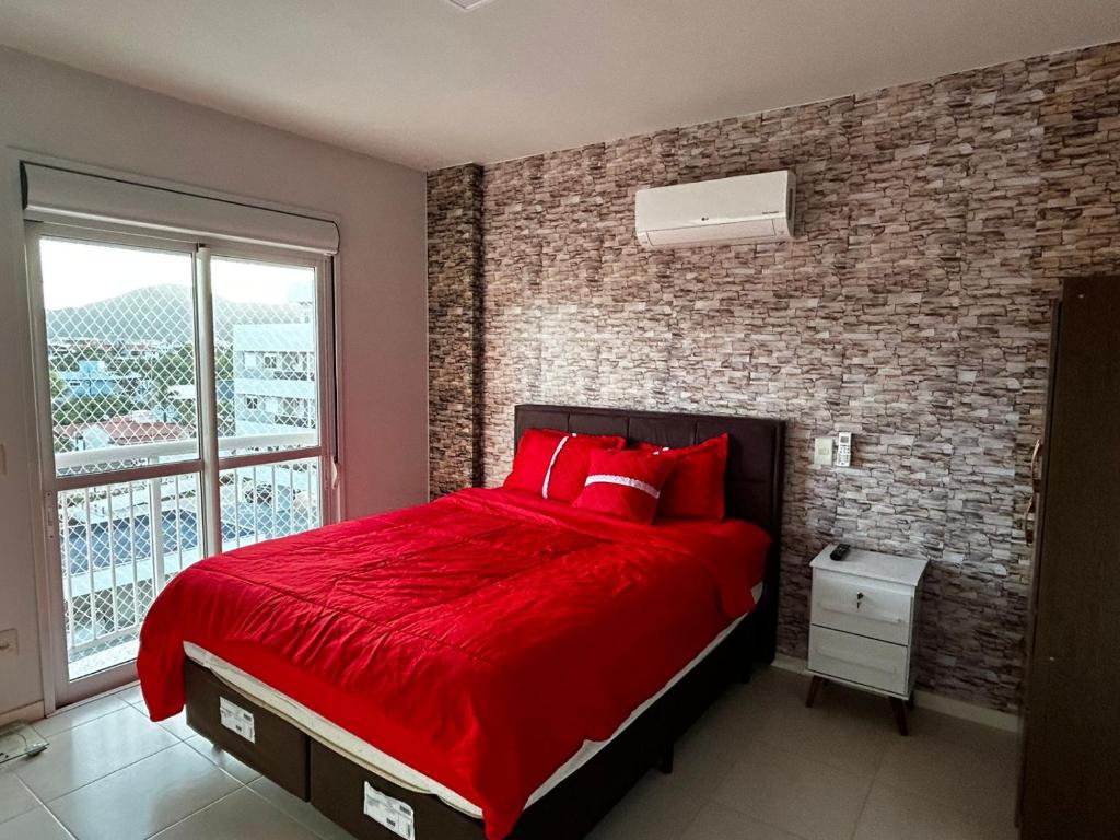 1 dormitorio con cama roja y pared de ladrillo en Cobertura Caju, en Florianópolis