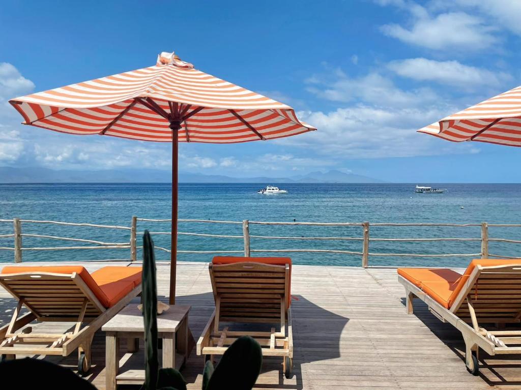 una terraza con sillas y sombrillas y el océano en VnS Beachfront Guesthouse en Nusa Penida