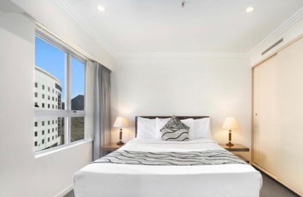 a white bedroom with a large bed and a window at Darling Harbour Apartments in Sydney