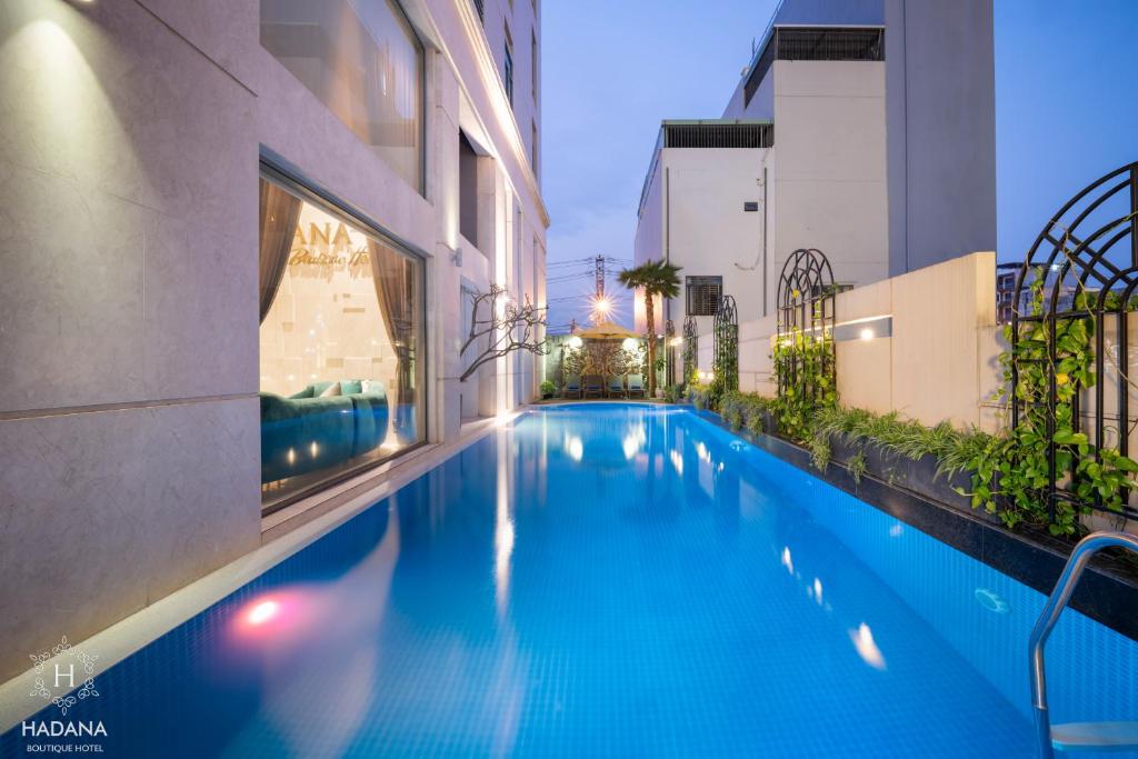 A narrow outdoor pool runs between hotel buildings and planted side walls at dusk.