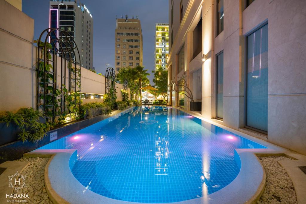 The illuminated pool stretches through a landscaped urban courtyard at night.