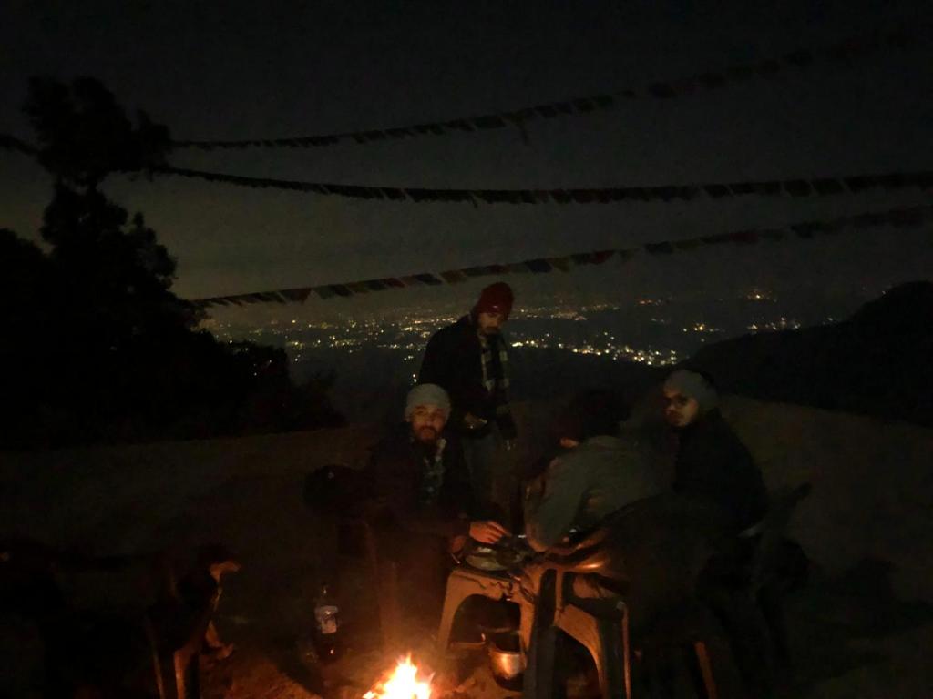 un grupo de personas sentadas alrededor de un fuego por la noche en Free style camps, en Mussoorie