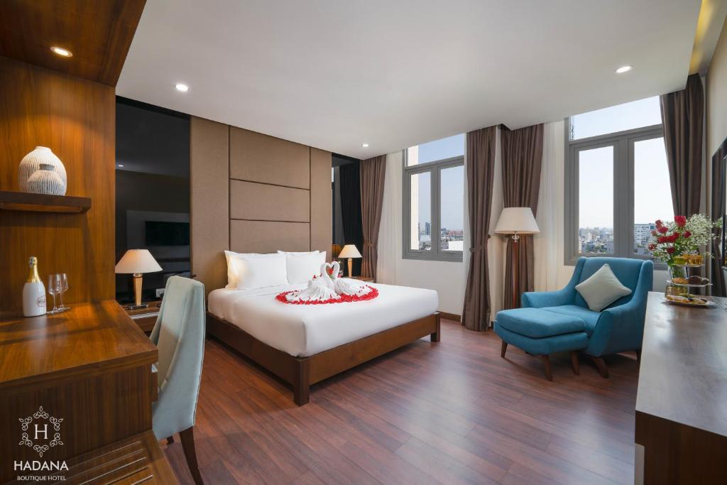 A bright bedroom with a large bed, blue armchair, desk and tall windows.
