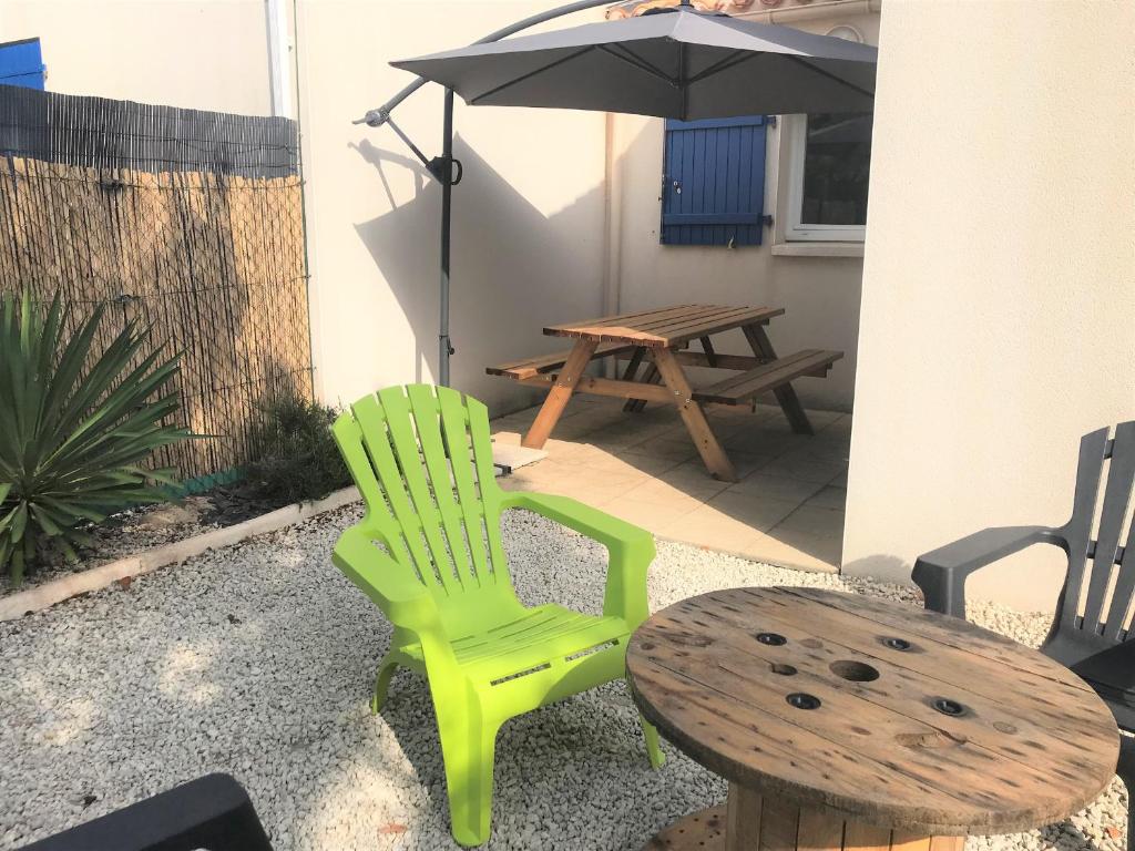 une terrasse avec une table, une chaise verte et un parasol dans l'établissement Charmante maisonnette à Longeville-sur-Mer, proche plage, 2 ch, terrasse, parking, vélos bienvenus - FR-1-22-311, à Longeville-sur-Mer