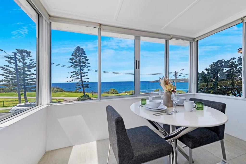 a dining room with a white table and chairs and windows at Ocean View 1 bedroom Private Apartment next to Maroubra Beach in Sydney