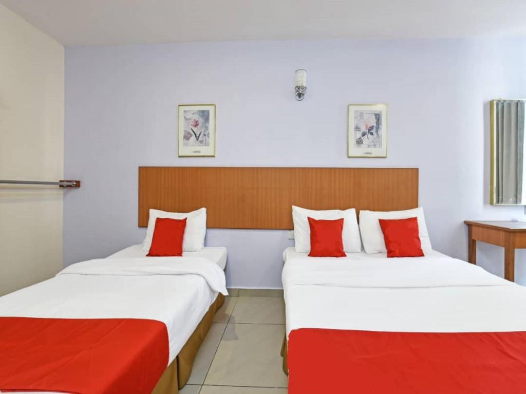two beds in a hotel room with red pillows at MRC Hotel Melaka Raya in Melaka