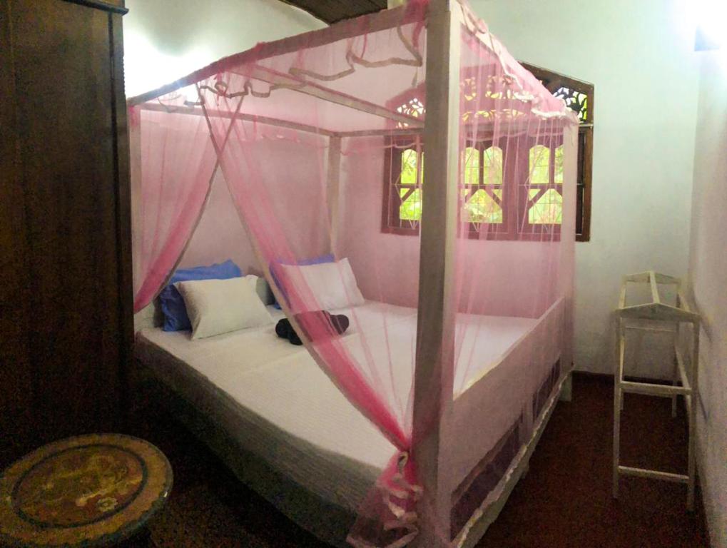 a bedroom with a canopy bed with pink drapes at Delight Homestay in Ahangama
