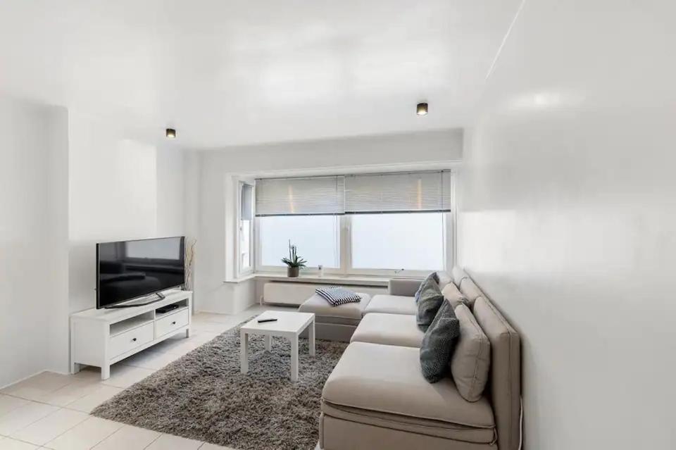 un soggiorno bianco con divano e TV di Sunny Apartment 500m from the beach Oostend a Ostenda